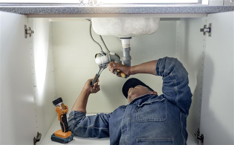 Plumber repairing pipes beneath a bathroom sink in Redondo Beach